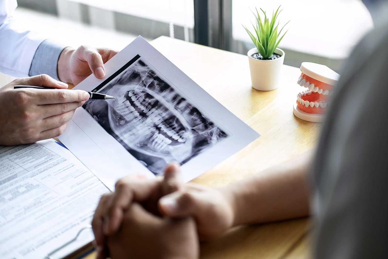 Periodontist showing tooth x-ray film and recommending treatment to his patient
